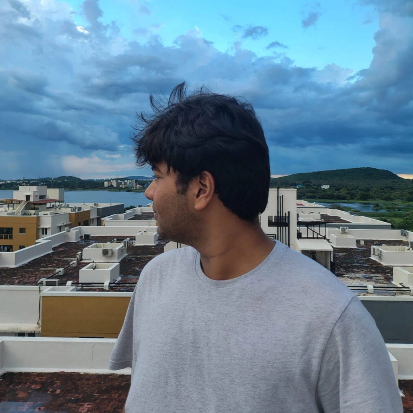 Sarthak Kumar on a rooftop, looking out over a lake and hills under a cloudy sky